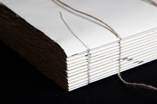 The process of book binding; close up of a raw book after sewing on cords. Black background