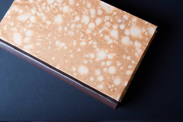 Art of Book binding; handmade book with marble paper front and leather book spine seen from above. Black background