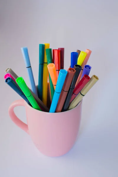 Pink cup full of colored markers. White background and copy space