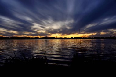 Karanlık mavi gökyüzü ve bahar akşamları gölün dalgalı sularında yansıyan büyülü günbatımı.