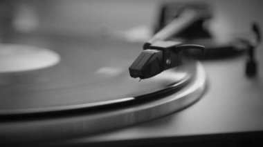 Siyah ve Beyaz. El, vinil plak açar. İğne vinil plaktan yükseliyor. Vinil plak dönüyor. İğne vinil plakla çalınıyor. Eski turntable