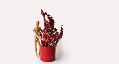 Holly kırmızı böğürtlen, Noel ışıklarına sarılı kırmızı vazoda duruyor. Noel ağacı farklı bir şekilde izole edilmiş. Tahta kukla Noel ağacı dallarına uzanıyor. Tatil dekorasyonları, ev ayarları