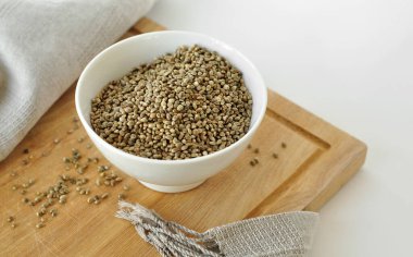 Tahta kesme tahtasındaki beyaz seramik kasede kenevir tohumları, keten havlu. Işık arka planında izole edilmiş. Esrar yemek pişirmede kullanılır. Yatay, gerçekçi görüntü