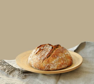 Yuvarlak ekşi ekmek, çıtır çıtır ekmek, un tozuyla kaplanmış, ahşap bir yüzeyde kırsal keten kumaş üzerinde dinleniyor. Ev yapımı fırın, geleneksel pişirme konsepti. Gerçekçi görüntü, Negatif boşluk