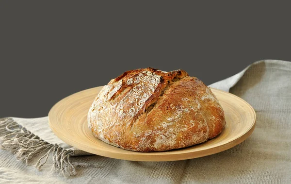 Yuvarlak ekşi ekmek, çıtır çıtır ekmek, un tozuyla kaplanmış, ahşap bir yüzeyde kırsal keten kumaş üzerinde dinleniyor. Ev yapımı fırın, geleneksel pişirme konsepti. Gerçekçi görüntü, Negatif boşluk