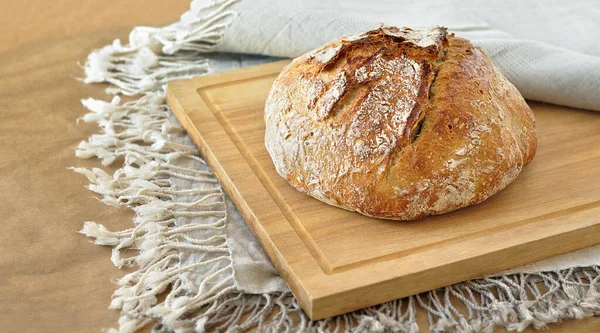 Yuvarlak ekşi ekmek, çıtır çıtır ekmek, un tozuyla kaplanmış, ahşap bir yüzeyde kırsal keten kumaş üzerinde dinleniyor. Ev yapımı fırın, geleneksel pişirme konsepti. Gerçekçi görüntü, Negatif boşluk