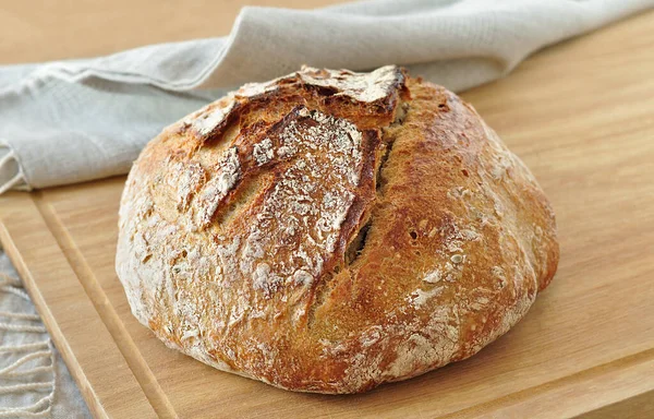 Yuvarlak ekşi ekmek, çıtır çıtır ekmek, un tozuyla kaplanmış, ahşap bir yüzeyde kırsal keten kumaş üzerinde dinleniyor. Ev yapımı fırın, geleneksel pişirme konsepti. Gerçekçi görüntü, Negatif boşluk