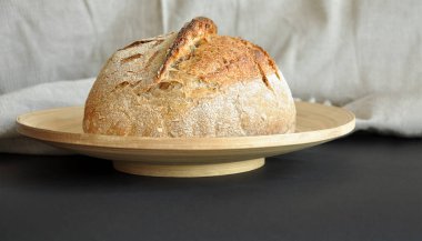Ekmek yapma eğilimi. Ekmek somunu, kırsal keten kumaş, bambu tepsisi, siyah arka plan. Un tozuyla kaplanmış gevrek ekmek kabuğu. Ev fırını, glütenli ürünler, geleneksel pişirme konsepti.