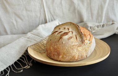 Ekmek yapma eğilimi. Ekmek somunu, kırsal keten kumaş, bambu tepsisi, siyah arka plan. Un tozuyla kaplanmış gevrek ekmek kabuğu. Ev fırını, glütenli ürünler, geleneksel pişirme konsepti.