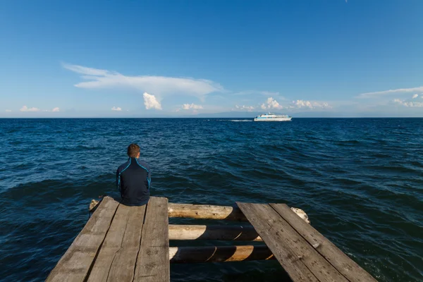 Man sitting on old wooden dock with Baikal lake view — Stock Photo, Image