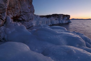 Baykal kayalık kıyısı gün batımında buzla kaplı.