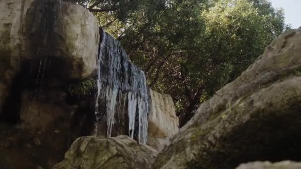 Een kleine waterval in de schaduw, de rotsen, de camera beweegt van links naar rechts. — Stockvideo