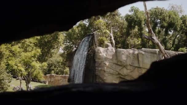 Een kleine sterke waterval in de verte in een kader van stenen. — Stockvideo