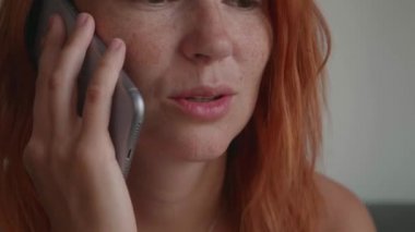 Kızıl saçlı bir kız telefonda konuşuyor, koltukta oturuyor, gülümsüyor.