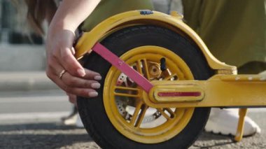 Genç bir kadın sokaktaki elektro scooter 'ın tekerleğini kontrol ediyor..