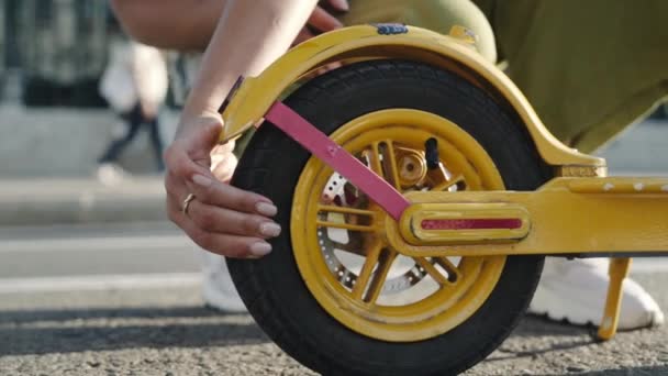 Uma jovem verifica a roda da scooter electro na rua. — Vídeo de Stock