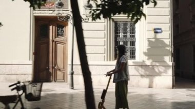 Bir kadın şehirde scooter 'a biniyor. Elektrikli scooter ile gidip gelmek