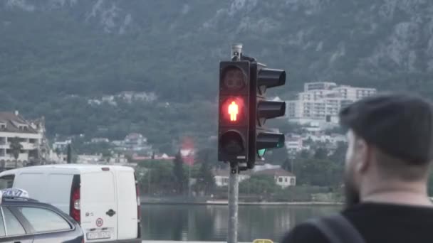 Un hombre con gorra espera la señal verde del semáforo. Montenegro. — Vídeo de stock