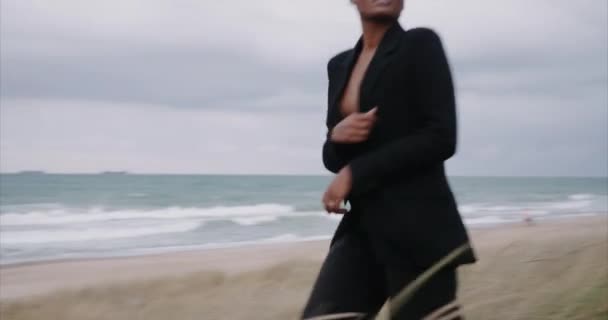 A black sexy girl in a jacket runs to the sea. Sunrise. — Stock Video