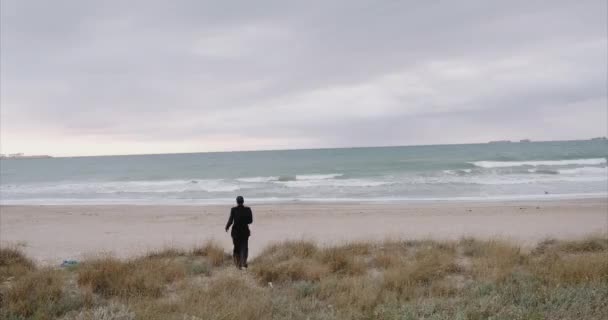 Una chica sexy negra con una chaqueta corre hacia el mar. Amanecer. — Vídeos de Stock