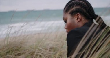 Kumsalda ceketli siyah seksi bir kız oturuyor. Gün doğumu.