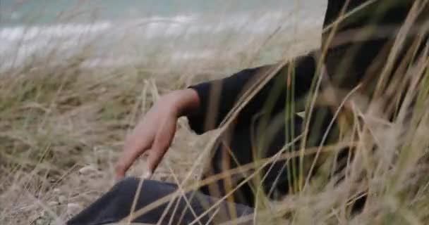 Uma menina sexy preta em uma jaqueta está sentada na praia. Nascer do sol. — Vídeo de Stock
