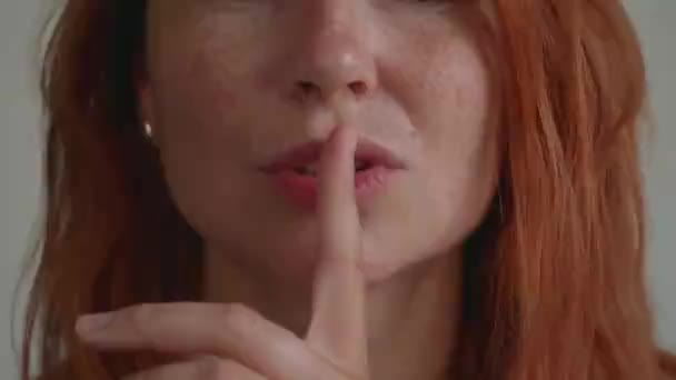 Ελκυστική νεαρή κοπέλα με κόκκινα μαλλιά. Βάζει ένα δάχτυλο στα χείλη του. — Αρχείο Βίντεο