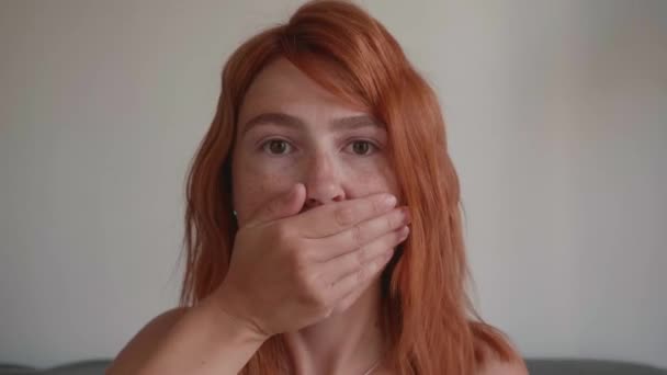 Attractive young girl with red hair. She covers her mouth with her hands. — Stock Video
