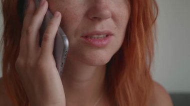 Kızıl saçlı bir kız telefonda konuşuyor, koltukta oturuyor, gülümsüyor.