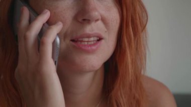 Kızıl saçlı bir kız telefonda konuşuyor, koltukta oturuyor, gülümsüyor.