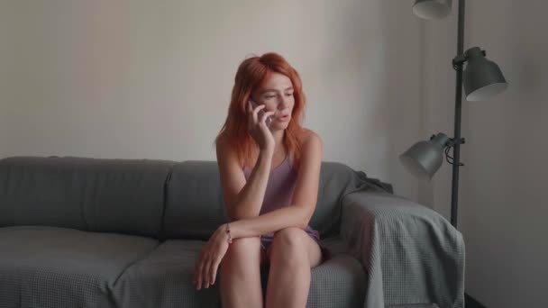 Девушка с рыжими волосами пользуется телефоном руками, сидя на диване. — стоковое видео