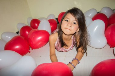 Pembe elbiseli bir kız balonların arasında eğleniyor..