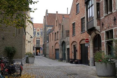 Bruges, Flanders, Belçika 10 18 2025 Cobblestone Avrupa sokağı eski tuğla binalar tarafından çerçevelenmiş. Bisikletler yan tarafa park edilmiş ve saksı bitkileri renk katıyor..