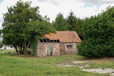 Zemin kattaki bir perspektiften yakalanan eski bir tuğla bina yeşil ağaçlar tarafından sarılmıştır. Mekan, kırsal kesimde terk edilme hissi uyandırıyor. Bina yaşlanma belirtileri gösteriyor..