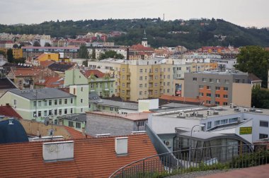 Brno Çek Cumhuriyeti Bu çekim çeşitli mimarisi ve çatıları olan bir Avrupa şehrini yakalar. Binaların renkleri ve yüksekliği farklıdır. Arka planda yeşil tepeler ve bulutlu bir gökyüzü vardır.. 