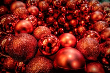 Yakından çekilmiş, kırmızı Noel süslemelerinin ışıltılı bir görüntüsü. Yansıtıcı süsler güzel bir parıltı yayar, bazıları parıltıyla süslenir, ayara bayram neşesi katar..