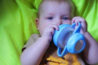 6 aylık yakın planda, mavi gözlü küçük bir çocuk sarı arka plandaki bir içiciden içki içiyor, yumuşak odaklı yatay görüntü, mesaj için yer