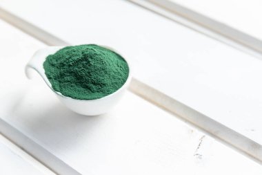 Beyaz ahşap bir masada yeşil spirulina tozu. Beyaz arka planda organik yeşil spirulina tozu. Süper yiyecekler. 2021. Besin takviyesi için vitamin, protein ve beta karoten. Dokunulmazlık desteği . 