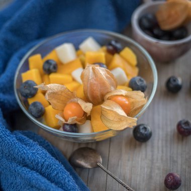 Mango parçalı meyve salatası ve cam kasede yaban mersini. Mavi bir bez üzerinde Phisalis. Fotokopi alanı olan meyve salatası 