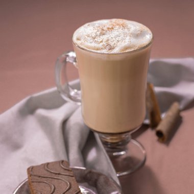 Bir fincan cappuccino, yanında da sinamon tozu ve tabakta kek. Bir fincan kahve ve mor arka planda gri bir peçete. Kafein. İyi sabahlar. Kahve zamanı. . 