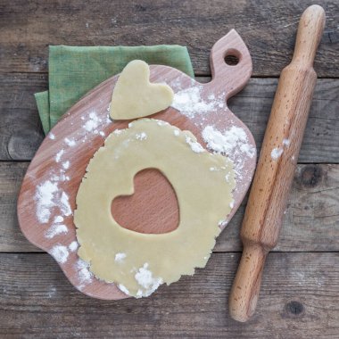  Kalp şeklinde hamur ve ahşap bir masanın üzerindeki kesme tahtasındaki merdane. Sevgililer günü, ev yapımı kurabiyeler. Kırmızı kalp .