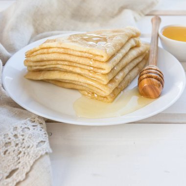 Krep, bal ve beyaz tabakta tahta bal kaşığı. Beyaz ahşap bir masada krep. Rus gözlemesi ve ballı üst görünüm . 