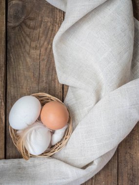 Küçük bir sepette tavuk beyazı ve kahverengi yumurta ve ahşap bir masada tüy. Çiğ yumurta ve ahşap bir masanın üzerinde fotokopi alanı olan bir peçete. Fotokopi alanı olan üst görünüm yumurtaları .