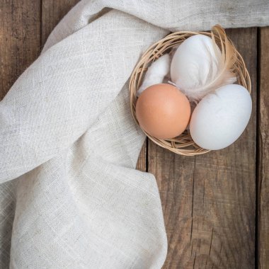 Küçük bir sepette tavuk beyazı ve kahverengi yumurta ve ahşap bir masada tüy. Çiğ yumurta ve ahşap bir masanın üzerinde fotokopi alanı olan bir peçete. Fotokopi alanı olan üst görünüm yumurtaları .