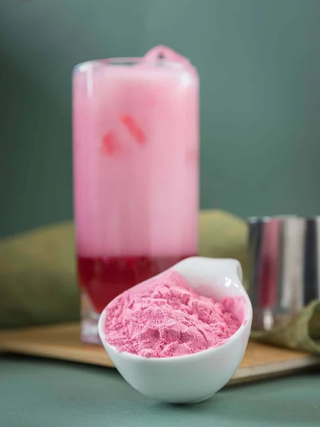 A glass of pink matcha ice drink . Pink matcha powder and  a glass of pink matcha iced latte  on a grey background .  Dragon fruit powder . Pitahaya powder drink . Summer drink .