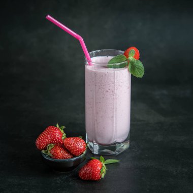 Siyah arka planda sütlü çilekli smoothie. Nane yapraklı bir bardakta ev yapımı çilekli milkshake. . 