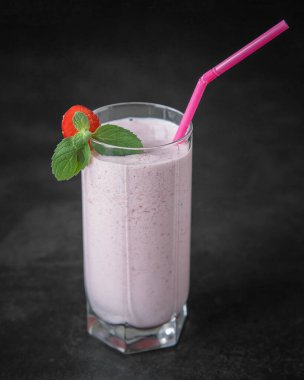 Siyah arka planda sütlü çilekli smoothie. Nane yapraklı bir bardakta ev yapımı çilekli milkshake. . 
