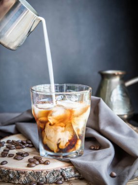 Sütlü buzlu kahve, gri bir peçeteye süt sürahisi, ahşap masa ve siyah arka plan. Tazeleniyor . 