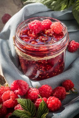 Reçel kavanozunda ev yapımı ahududu reçeli, gri peçetede çiğ ahududu. Doğal tatlı. Çiftçilik. Bahçe ahududu .  
