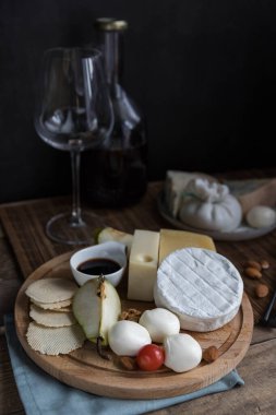 Siyah arka planda peynir tahtası ve asma. Karışık peynir, fındık ve armut. Parmesan, camembert, brie, mozzarella ve Masdam siyah arka plan manzaralı. Peynir dükkanı. Peynir menüsü . 